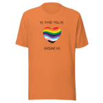 The image shows a unisex crew neck burnt orange t- shirt with a minimalist yet vibrant design. Centered on the front is a heart-shaped graphic filled with horizontal stripes in the colors of the progressive Pride flag, symbolizing inclusivity and diversity. Above the heart, the text reads "BE WHO YOU BE" and below it, "AROUND ME" both in sleek, black font. The design conveys an authenticity, making this t-shirt a wearable statement for equality and individuality.