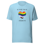The image shows a unisex crew neck ocean blue t- shirt with a minimalist yet vibrant design. Centered on the front is a heart-shaped graphic filled with horizontal stripes in the colors of the progressive Pride flag, symbolizing inclusivity and diversity. Above the heart, the text reads "BE WHO YOU BE" and below it, "AROUND ME" both in sleek, black font. The design conveys an authenticity, making this t-shirt a wearable statement for equality and individuality.