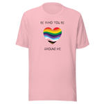 The image shows a unisex crew neck pink t- shirt with a minimalist yet vibrant design. Centered on the front is a heart-shaped graphic filled with horizontal stripes in the colors of the progressive Pride flag, symbolizing inclusivity and diversity. Above the heart, the text reads "BE WHO YOU BE" and below it, "AROUND ME" both in sleek, black font. The design conveys an authenticity, making this t-shirt a wearable statement for equality and individuality.