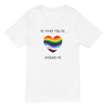 The image shows a unisex V-neck white t-shirt with a minimalist yet vibrant design. Centered on the front is a heart-shaped graphic filled with horizontal stripes in the colors of the progressive Pride flag, symbolizing inclusivity and diversity. Above the heart, the text reads "BE WHO YOU BE" and below it, "AROUND ME" both in sleek, black font. The design conveys an authenticity, making this t-shirt a wearable statement for equality and individuality.