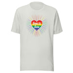 A silver crew neck unisex t-shirt featuring a design of a vibrant rainbow-striped heart at the center with the text "love is love" written inside. Around the heart colorful, radiating lines, with sunburst effect emphasizing inclusivity and love for all.