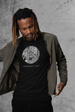 A model with brown skin tone is wearing a unisex black crew-neck t-shirt with a circular graphic design in the center of the chest. Inside the circle is a detailed black- and-white map depicting the streets and layout of Minneapolis. At the center of the map, a solidarity fist symbol. Below the circular map, in bold white text, the t- shirt reads, "MINNEAPOLIS, 2020." The model is also wearing casual green jacket over this t-shirt creating a comfortable casual look. 
